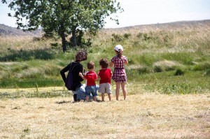 Tres niños y una chica en la orilla del estanque, de espaldas, esperando ver alguna rana.