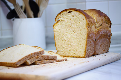 Delicioso pan de molde hecho de leche en una tabla de madera con tres rebanadas cortadas al lado
